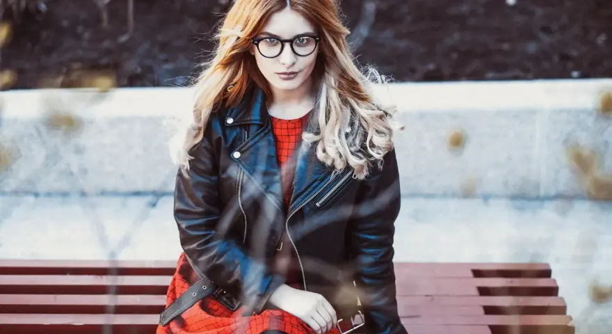 Dziewczyna w okularach i czerwonej sukience siedzi na ławce, ubrana w stylową kurtkę Dolce & Gabbana.