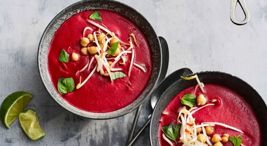 Zwei Schalen cremiger, **roter Bete Suppe mit Kokosmilch und Orangensaft**, garniert mit Kichererbsen und Sprossen.