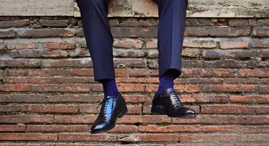 Uomo con calzini blu a pois bianchi e scarpe nere lucide. Un perfetto abbinamento calzini scarpe uomo per un look elegante.