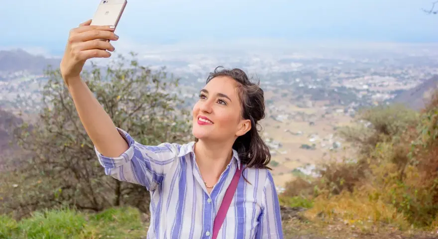 Uśmiechnięta dziewczyna robi selfie na tle miasta. Idealne zdjęcie na portal randkowy.