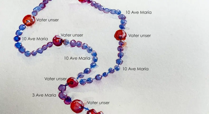 Ein Rosenkranz mit blauen und roten Perlen, beschriftet mit "Vater unser" und "Ave Maria". Die Rosenkranz Kette Bedeutung liegt in der Meditation und dem Gebet.