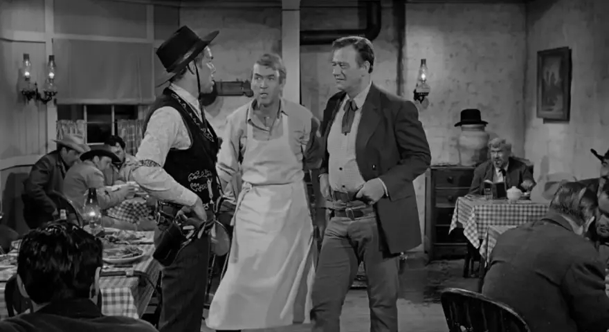 Inquadratura americana di tre uomini in un saloon. Uno indossa un grembiule, gli altri abiti western.