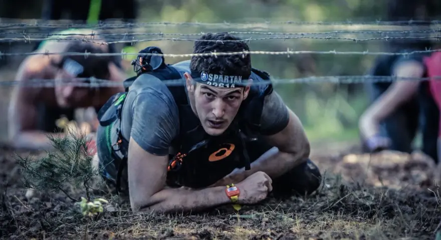 En man kryper under taggtråd under ett ocr sport-lopp.