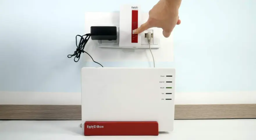 Finger drückt Knopf am Fritz!Repeater, um das **wifi repeater einrichten** zu starten. Fritz!Box steht daneben.