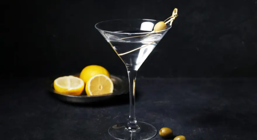 En klassisk vodka martini med en oliv på en tandpetare. Citroner ligger på en tallrik i bakgrunden.