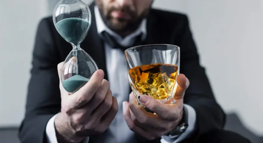 Mann im Anzug hält Sanduhr und Whiskyglas. Die Frage, ob kann Whisky schlecht werden, wird durch die vergehende Zeit und den edlen Tropfen symbolisiert.