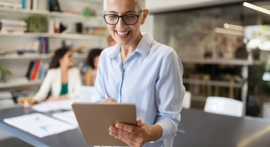 A smiling woman reviews a board chair job description on a tablet in a modern office.