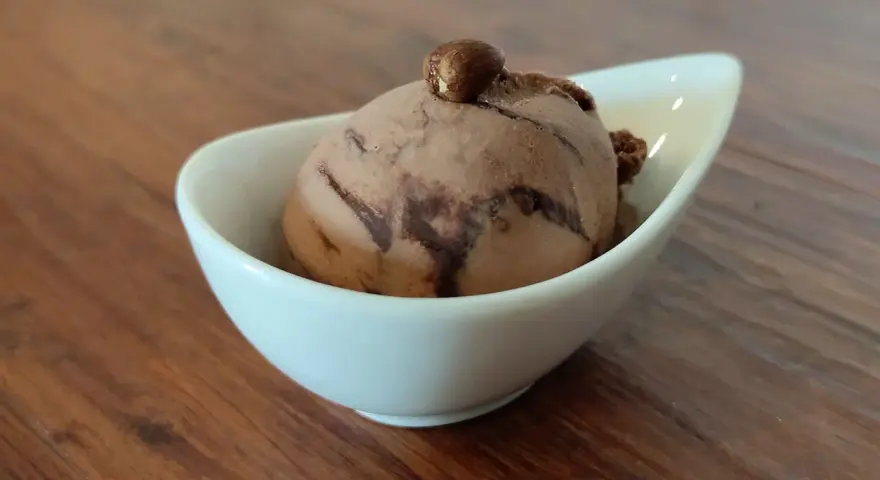 Ein Bacio Eis in einer weißen Schale, gekrönt von einer Haselnuss. Ein süßer Genuss auf Holztisch.