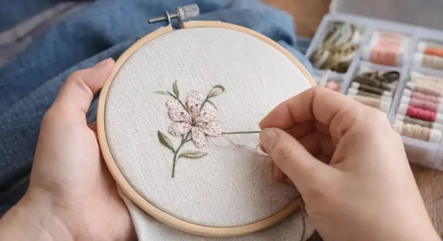 Manos bordando una flor en un bastidor. Se aprecian hilos de colores y las medidas de los bastidores son importantes para este arte.