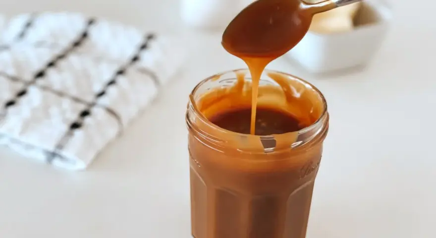 Une cuillère verse du caramel onctueux dans un pot. La recette caramel parfaite pour vos desserts.