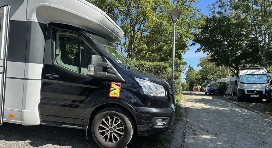 Husbil parkerad på en campingplats vid frankrike kust. Soligt väder med träd och andra husbilar i bakgrunden.