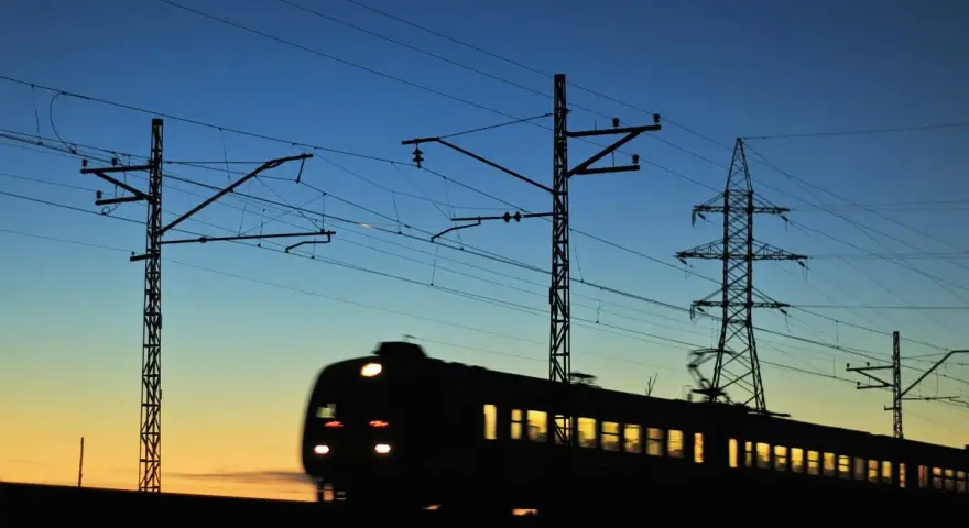 Pociąg w ruchu na tle zachodzącego słońca i linii energetycznych.
