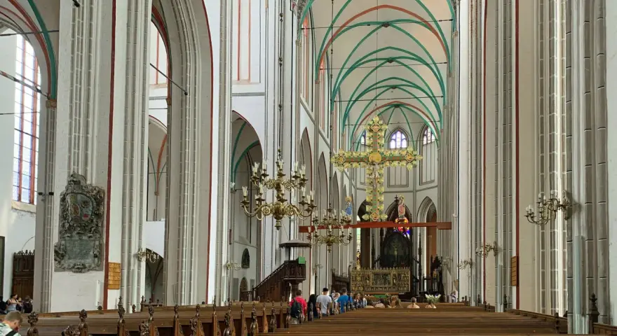 Imposanter Innenraum des Schweriner Doms mit Holzbänken, einem großen goldenen Kreuz und grünen Gewölben.