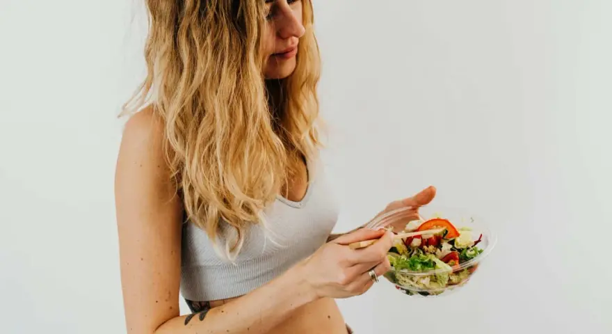 Donna con capelli biondi mangia un'insalata fresca, parte della sua vlckd dieta.