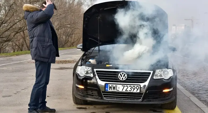 Mężczyzna z przerażeniem patrzy na dymiący silnik swojego Volkswagena. To typowe objawy zatarty silnik.