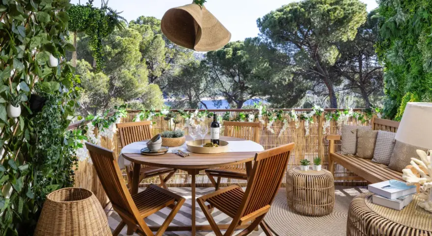 Encantadora decoracion terrazas con mesa de madera, sillas, banco y mucha vegetación. Un oasis verde para disfrutar del aire libre.