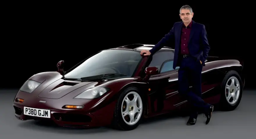 Rowan Atkinson w garniturze opiera się o swój bordowy McLaren F1. To jeden z jego ulubionych samochodów.