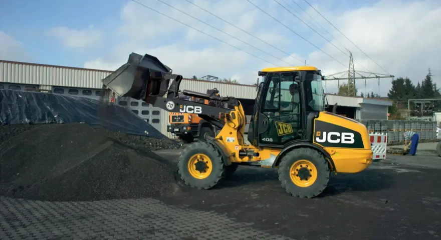 Żółta ładowarka JCB 406 z podniesioną łyżką, gotowa do pracy. Dane techniczne tej maszyny pozwalają na efektywne przenoszenie materiałów.