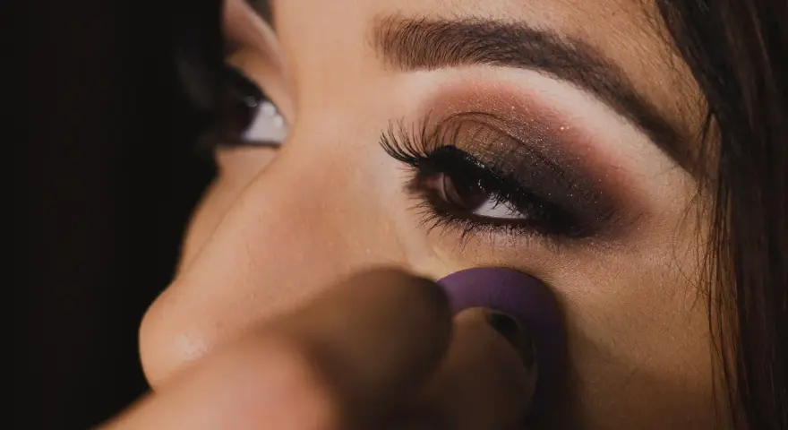 Un œil maquillé avec un smoky eyes facile, rehaussé de paillettes. Une éponge violette est utilisée pour estomper le fond de teint.