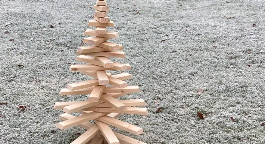 Ein selbstgemachter Tannenbaum aus Holz, der auf frostigem Gras steht. Eine rustikale Deko-Idee, um den Winter zu begrüßen.