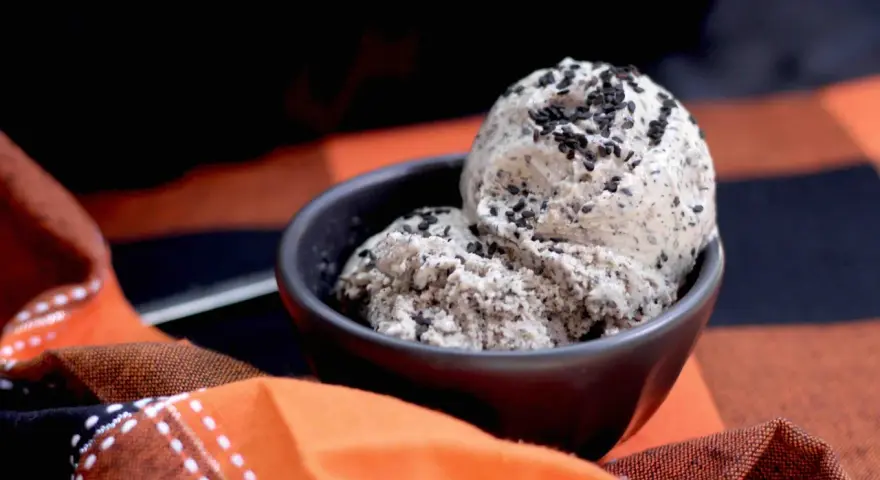 Zwei Kugeln cremiges **black sesame ice cream** in einer Schale, bestreut mit schwarzen Sesamsamen, auf einem karierten Stoff.