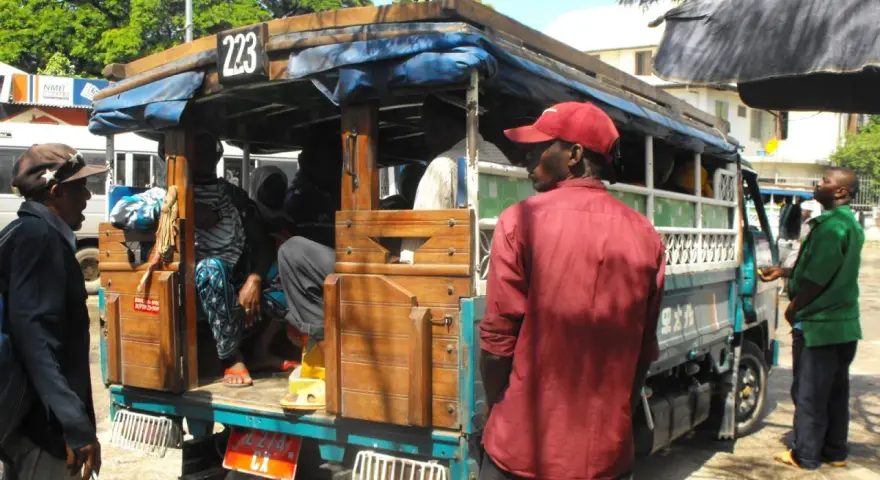 Ludzie wsiadają do dala dala na Zanzibarze. Widać drewnianą konstrukcję pojazdu i pasażerów.