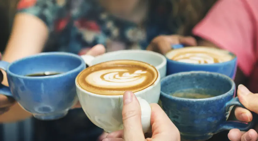 Vier Hände halten bunte Kaffeetassen. Der Kaffee reizt die Blase, aber der Genuss ist es wert.