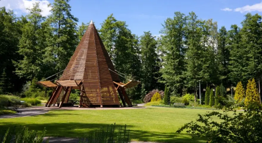 Drewniana konstrukcja w kształcie stożka na tle zielonej góry i lasu. Idealne miejsce na spacer.