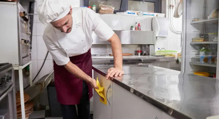 Cocinero con delantal limpiando encimera de acero inoxidable. Esencial para la limpieza de restaurantes.
