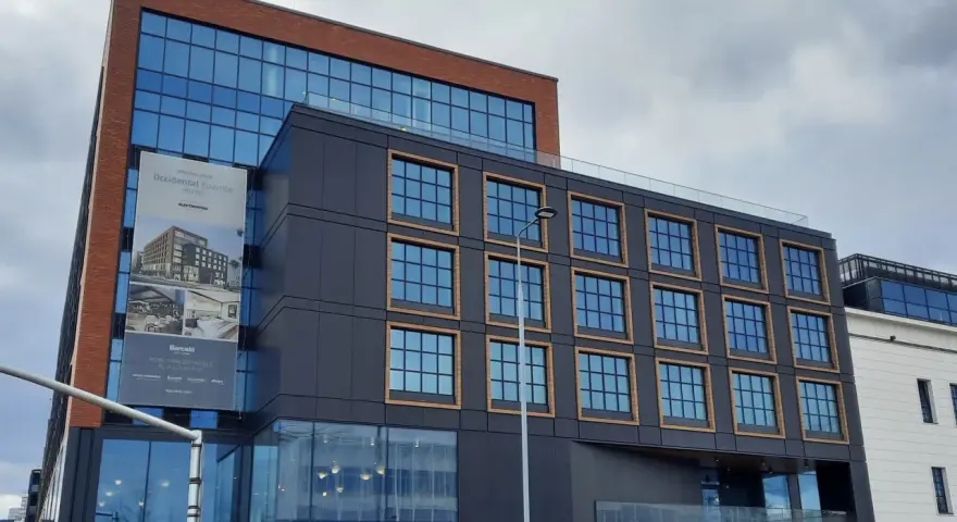 Nowoczesny budynek z cegły i ciemnej fasady, z banerem zapowiadającym otwarcie Occidental Powisle Hotel, części sieci Barceló.