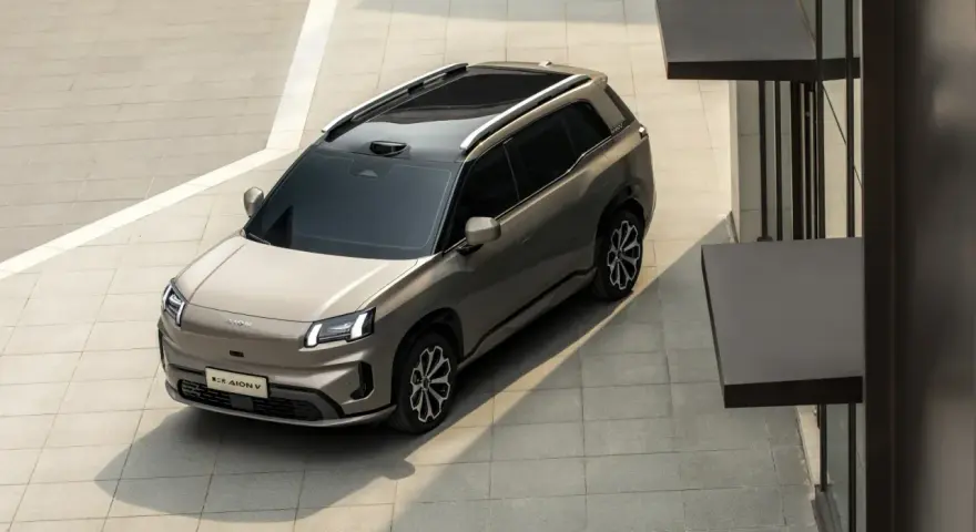 Szary elektryczny SUV GAC Aion V z czarnym dachem i relingami, zaparkowany na zewnątrz.