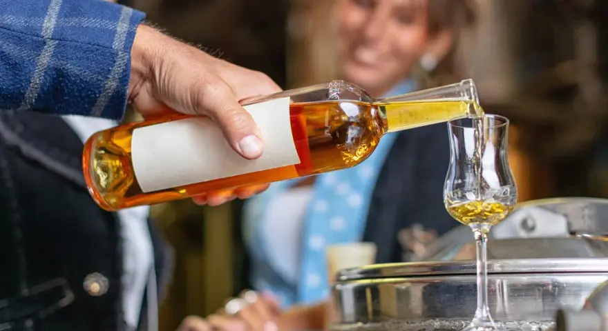 Mężczyzna nalewa złocisty grappa alkohol do kieliszka. W tle uśmiechnięta kobieta.