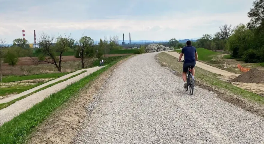 Mężczyzna na rowerze przemierza nową ścieżkę rowerową w Skawinie. W tle widać przemysłowe kominy i zielone tereny.