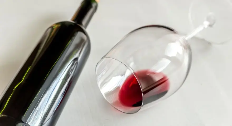 Ciemna butelka i przewrócony kieliszek z czerwonym winem. Idealny wieczór z winem półwytrawnym.