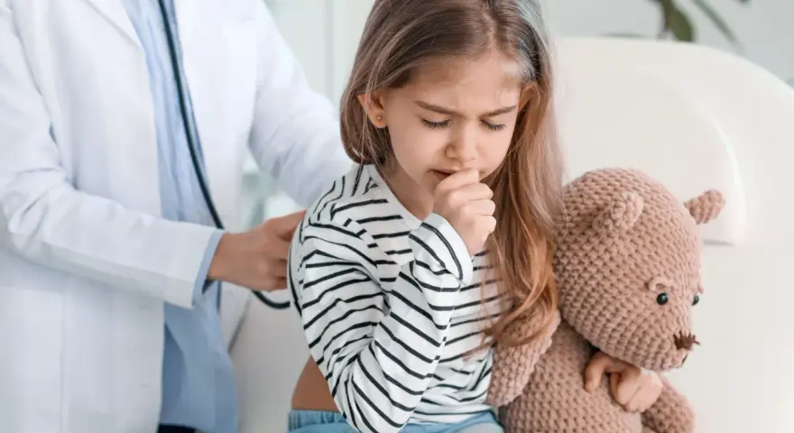 Lekarz bada dziecko z duszącym kaszlem. Dziewczynka przytula misia, czując się źle.