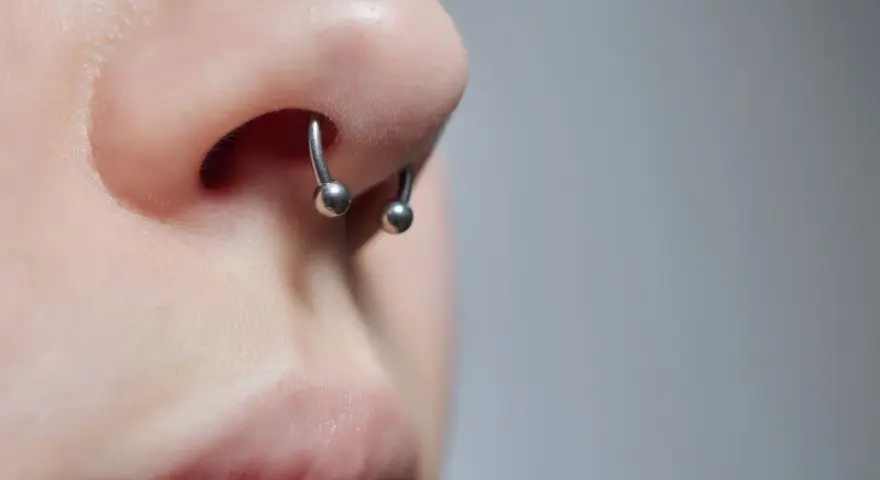 Zbliżenie na nos z kolczykiem typu septril piercing. Metalowy okrąg z dwoma kulkami subtelnie zdobi przegrodę nosową.