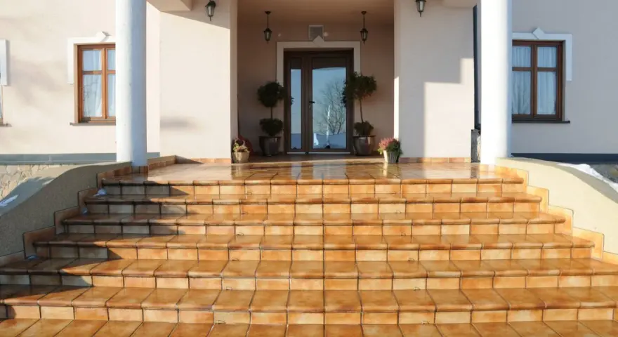 Amplias escaleras exteriores para casas de dos pisos, con escalones de baldosas naranjas que conducen a una entrada principal.