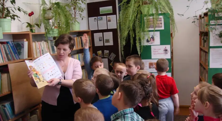 Nauczycielka czyta dzieciom książkę, tworząc inspirujące lekcje biblioteczne scenariusze. Dzieci słuchają z uwagą.