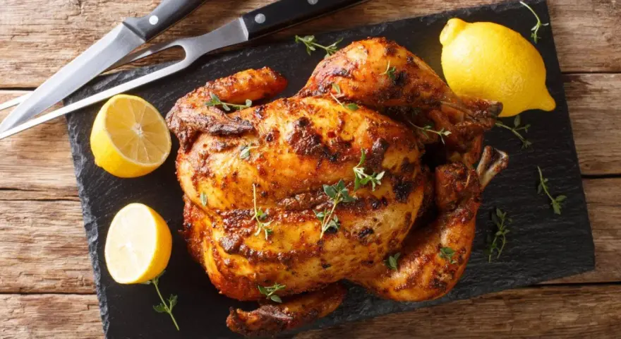 Pollo al horno dorado y jugoso, adornado con tomillo fresco y acompañado de limones cortados. Un festín listo para servir.