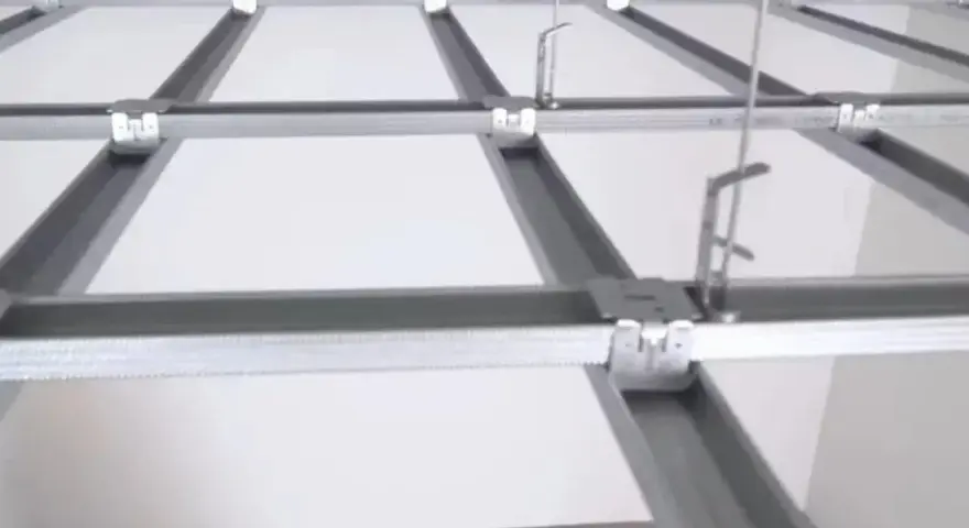 Sufit podwieszany krzyżowy z białymi panelami i metalową konstrukcją. Widać system profili, który tworzy siatkę, a nie pojedyncze belki.