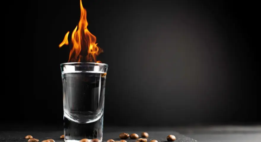 Ein Schnapsglas mit brennendem Sambuca und Kaffeebohnen. Die Flammen tanzen, ein Spektakel, das erklärt, warum brennt Sambuca.