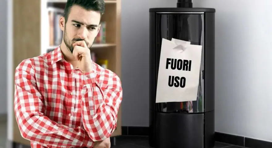 Uomo pensieroso guarda stufa spenta con foglio "FUORI USO". Necessaria riparazione stufe per il freddo.