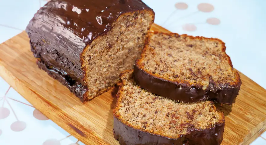 Saftiger Kuchen mit Bananen und Schokoladenglasur, auf einem Holzbrett serviert.