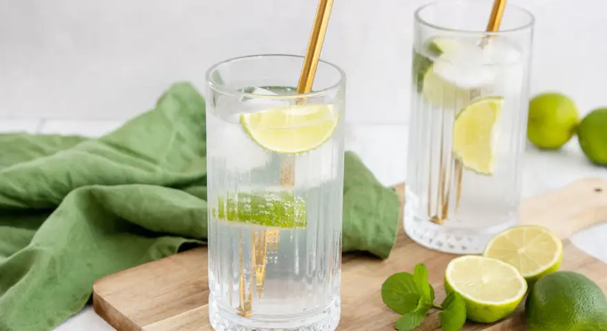 Erfrischende Drinks: Zwei Gläser mit Eis, Limettenscheiben und goldenen Strohhalmen. Perfekt zum **Wodka mischen** an einem warmen Tag.