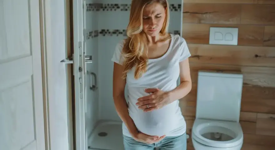 Kobieta w ciąży z wyrazem bólu na twarzy trzyma się za brzuch. Może to być ból podbrzusza w ciąży.