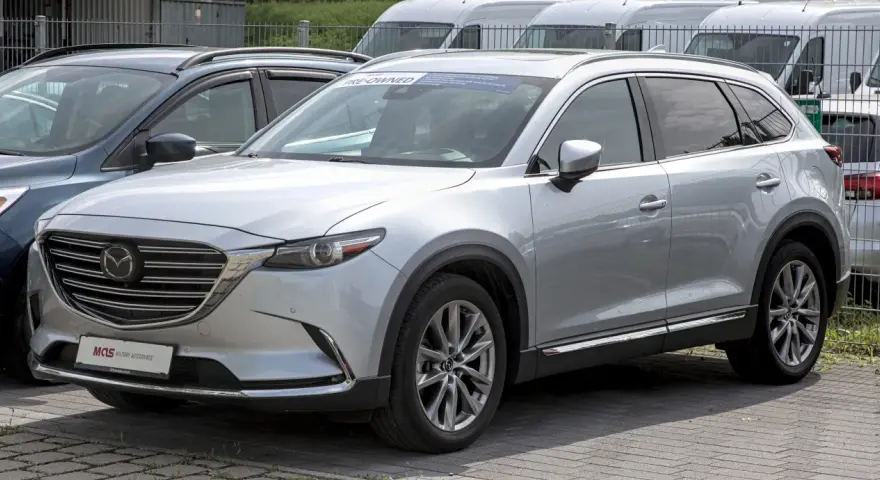 Srebrna Mazda CX-9 z napisem "PRE-OWNED" na przedniej szybie, zaparkowana na zewnątrz.