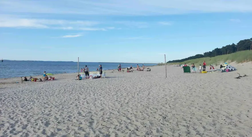 Menschen entspannen sich am sonnigen Lubmin Strand. Das Meer glitzert, der Himmel ist blau mit leichten Wolken.