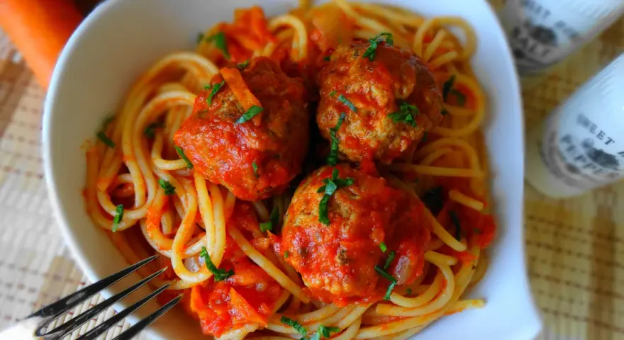 Pyszne spaghetti z klopsikami w sosie pomidorowym, posypane natką pietruszki. Idealne danie dla całej rodziny.
