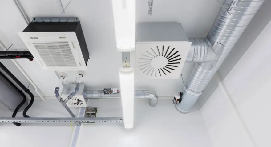 Detalles de sistemas de ventilación y extracción de aire, incluyendo conductos metálicos, unidades de aire acondicionado y luces fluorescentes en un techo.