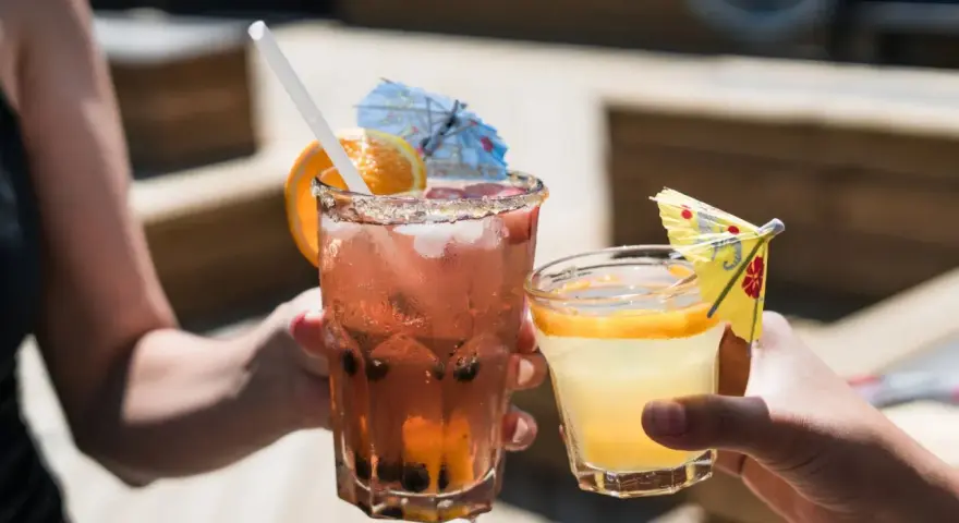 Dwa orzeźwiające drinki, jeden różowy z owocami i pomarańczą, drugi żółty z plasterkiem pomarańczy. Idealne na letnie popołudnie, może z dodatkiem białego wina.
